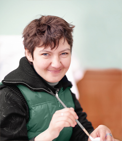 A photo of a smiling resident with a paintbrush in her hand